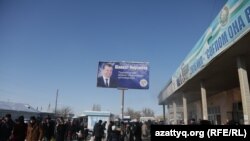 Люди проходят мимо рекламного щита возле базара, надпись на узбекском языке гласит: «Предприниматели поддерживают Шавката Мирзиёева». Ташкентская область, 27 ноября 2016 г.