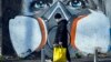 ITALY -- A man walks with his groceries beside a mural painting that portrays a person wearing a gas mask, Milan, Italy, 16 March 2020. 