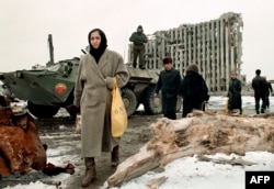 Чечня. Чеченские женщины и мужчины проходят мимо бронетранспортера российской армии в феврале 1996 года перед разрушенным президентским дворцом в Грозном