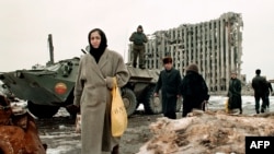 Chechnya -- Chechen women and men pass in February 1996 by a Russian Army armoured personnel carrier in front of destroyed presidential palace in Grozny, capital of the breakaway southern republic of Chechnya. Russian troops entered Chechnya 11 December 1