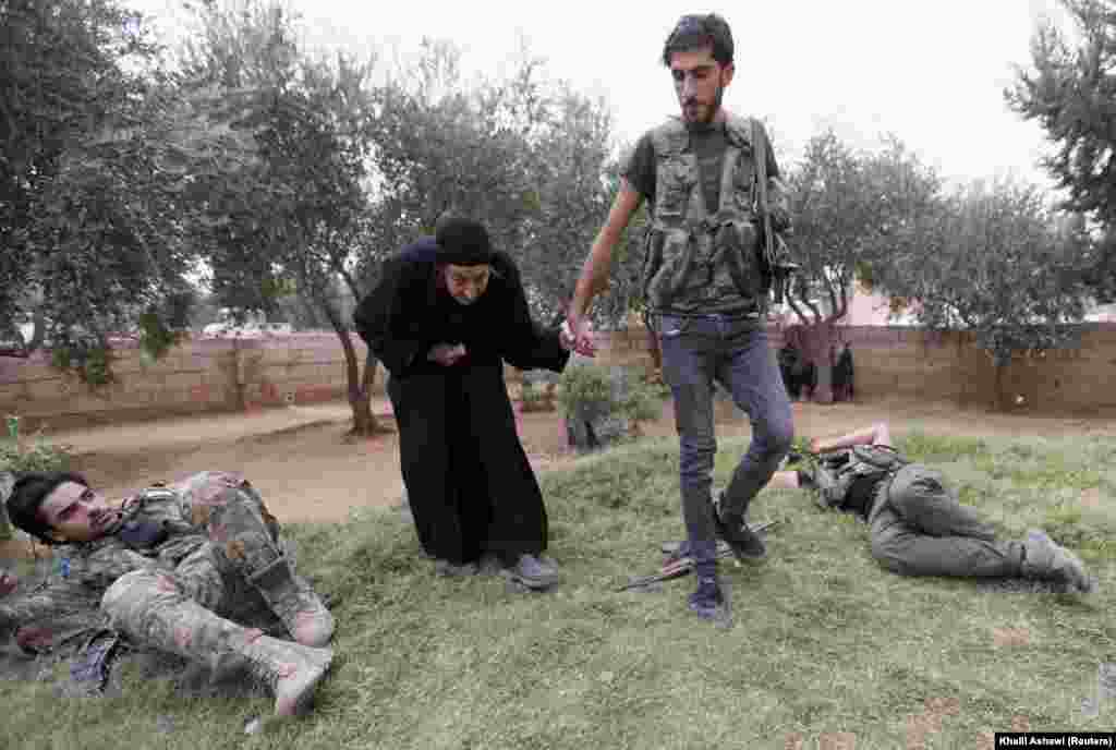 A Turkish-backed Syrian rebel fighter walks an elderly woman past fellow resting combatants near the border town of Tal Abyad on October 24. (Reuters/Khalil Ashawi)