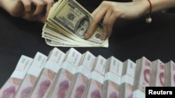 Пачки банкнот номиналом 100 юаней и доллары США. Иллюстративное фото.