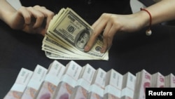 An employee counts U.S. dollars next to yuan banknotes at a bank in Hefei, in China's Anhui Province.