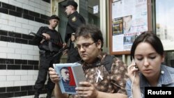 Russian security forces stand guard as an opposition supporter and Anna Veduta (right), a spokeswoman for opposition activist Aleksei Navalny, wait outside the entrance to the apartment block where Navalny lives in Moscow on June 11.