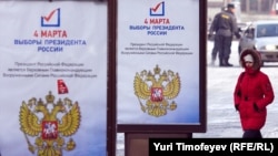 A woman passes by a presidential election campaign posters in Moscow