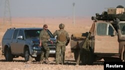 U.S. servicemen stand near military vehicles, north of Raqqa, in Syria earlier this month