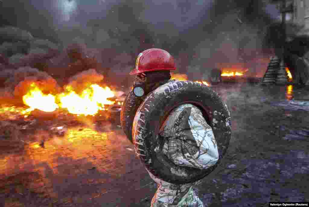 A protester carries tires to add to a burning pile at the site of clashes with riot police.