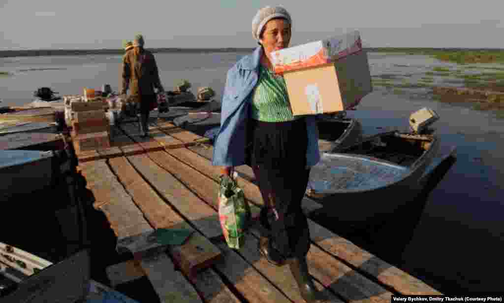 A shop assistant brings supplies to a village shop that have been delivered by boat.