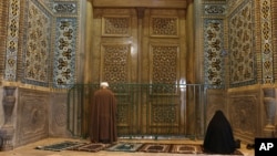 A cleric and a woman pray behind a closed door of Masoume shrine in the city of Qom, some 80 miles (125 kilometers) south of the capital Tehran, Iran, Monday, March 16, 2020