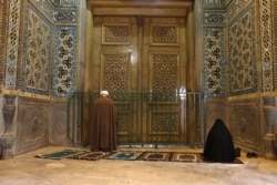 IRAN - A cleric and a woman pray behind a closed door of Masoume shrine in the city of Qom, some 80 miles (125 kilometers) south of the capital Tehran, Iran, Monday, March 16, 2020