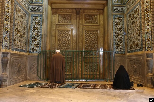 IRAN - A cleric and a woman pray behind a closed door of Masoume shrine in the city of Qom, some 80 miles (125 kilometers) south of the capital Tehran, Iran, Monday, March 16, 2020