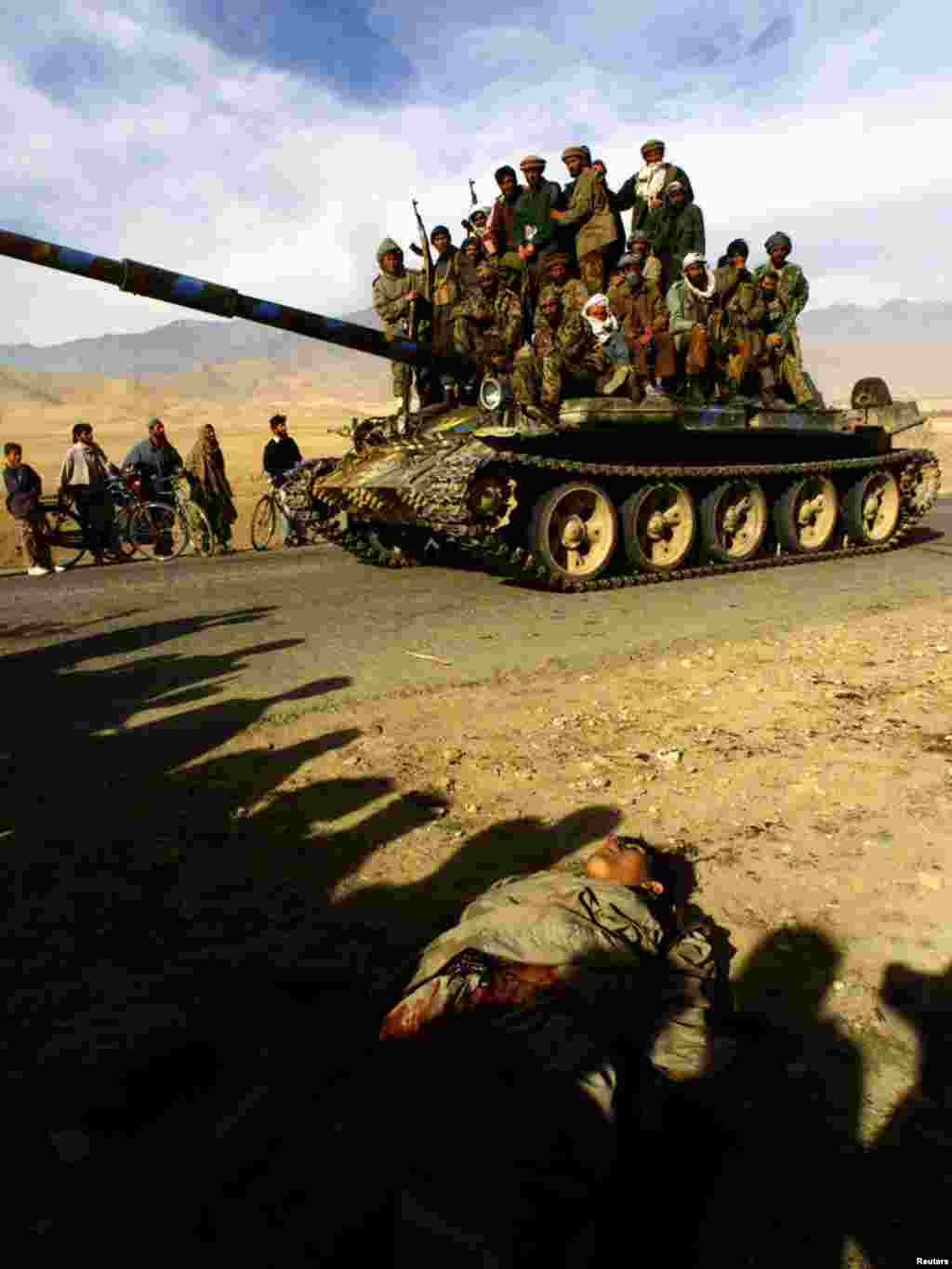 Northern Alliance fighters ride on a T-62 tank past a dead body on the motorway 3 km north of Kabul, as Northern Alliance fighters approached the Afghan capital, November 13, 2001. Forces of the anti-Taliban Northern Alliance entered Kabul on Tuesday after Taliban forces fled the capital, and were greeted by civilians. REUTERS