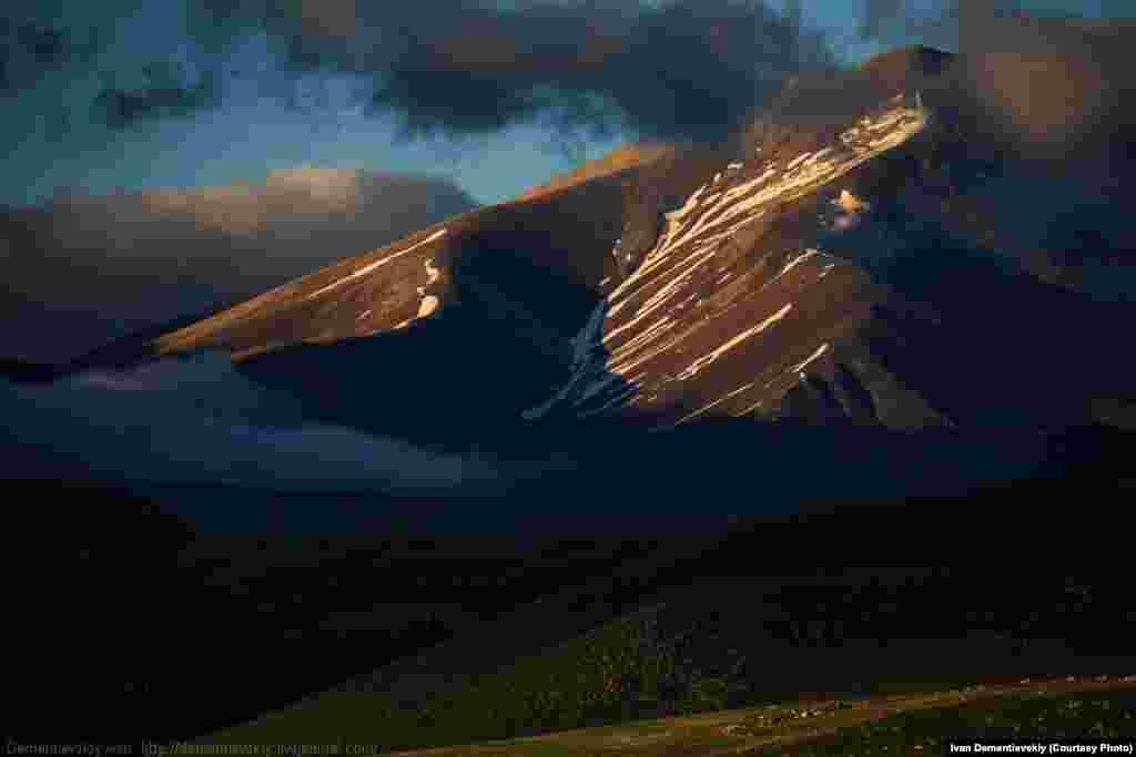 The last rays of evening light cast a long shadow over the mountains. Snow is still visible from winters past. 