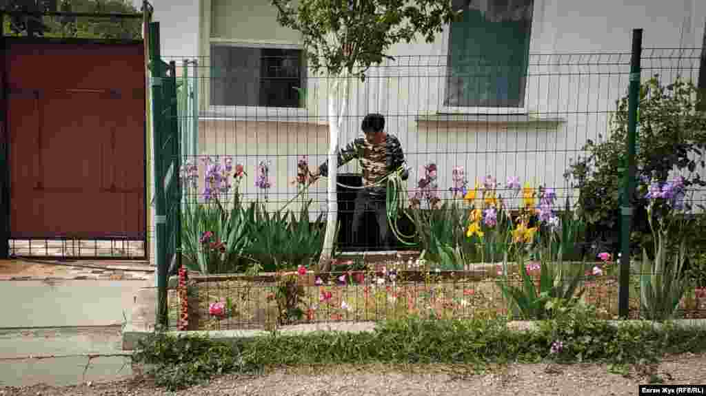 У частного дома мужчина поливает цветы в палисаднике