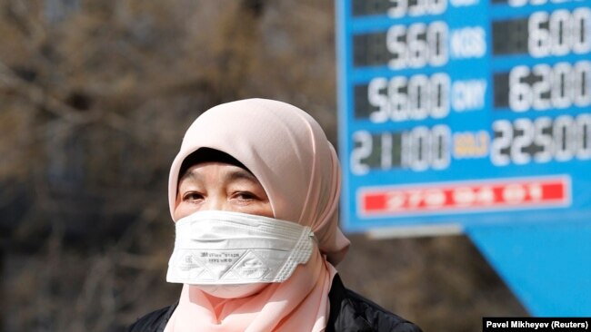 Женщина в маске рядом с электронным табло пункта обмена валют в Алматы. 16 марта 2020 года.