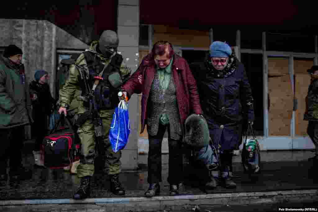 Украинский военнослужащий помогает пожилым женщинам спуститься по лестнице