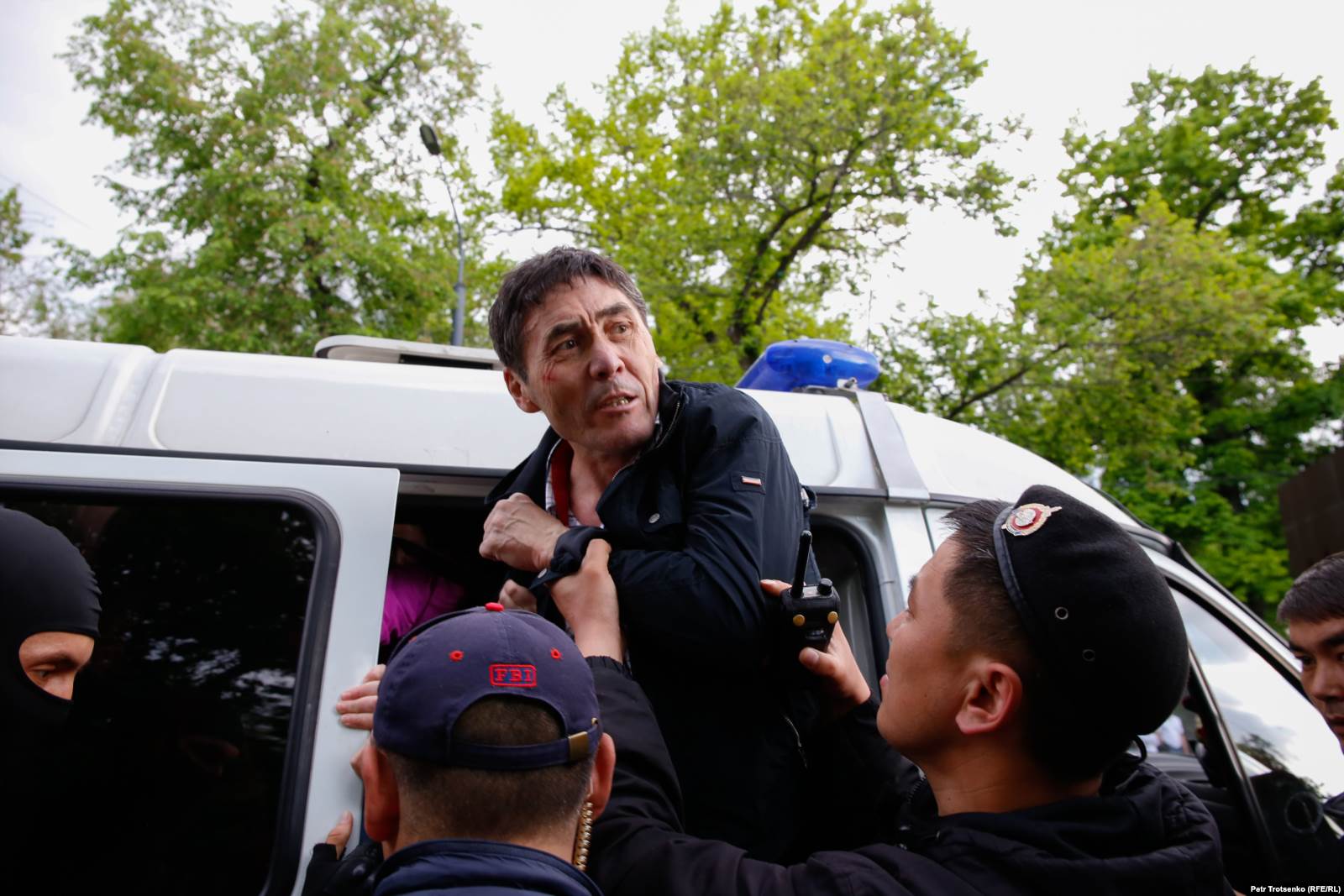 Полиция ұсталған адамдардың бірін шағын автобусқа салып жатыр.