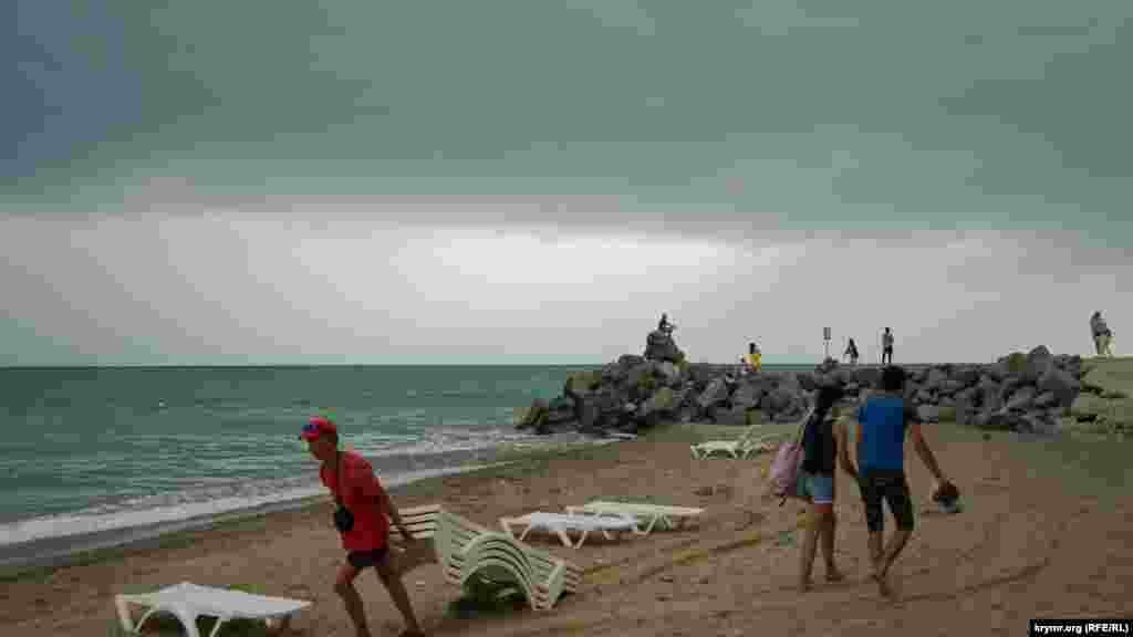 Работники пляжа убирают шезлонги перед дождем