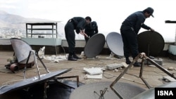 Иранские полицейские демонтируют спутниковые антенны, установленные на крыше здания.