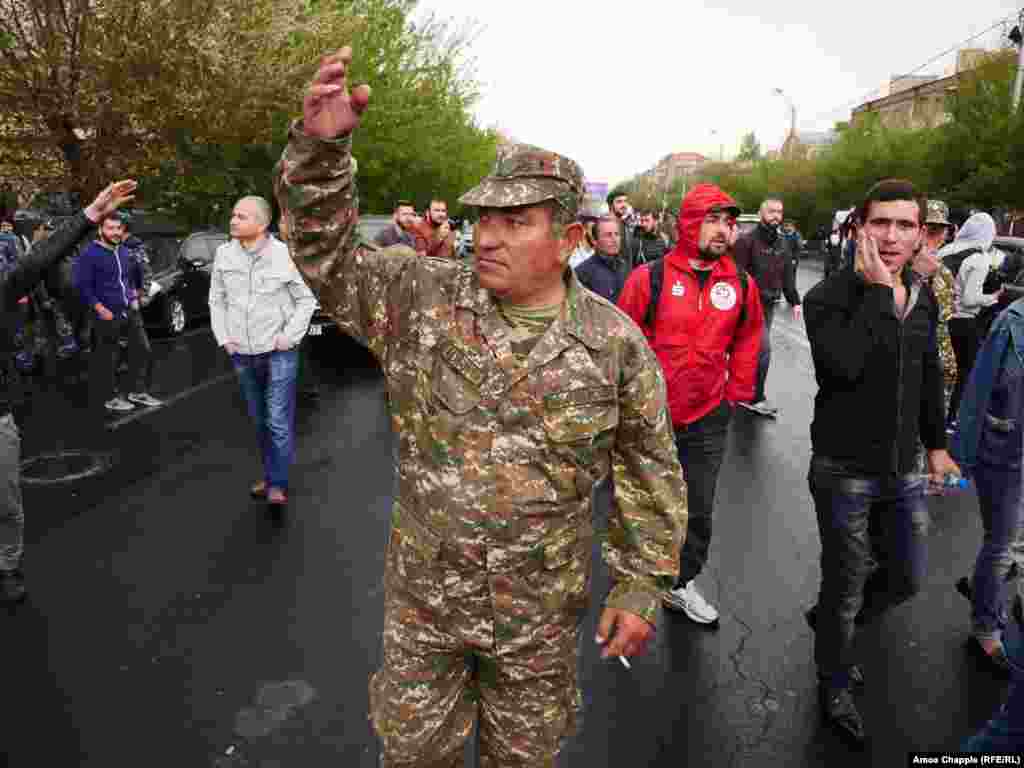 A man wearing an Armenian army uniform gestures at a line of police, encouraging them to join the protest.