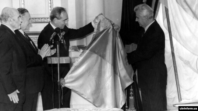 Синьо-жовтий прапор – символ державності уряду Української Народної Республіки – вручає в Маріїнському палаці президенту України Леоніду Кравчуку останній президент УНР в екзилі Микола Плав’юк. Київ, 22 серпня 1992 року Синьо-жовтий прапор – символ державності уряду Української Народної Республіки – вручає в Маріїнському палаці президенту України Леоніду Кравчуку останній президент УНР в екзилі Микола Плав’юк. Київ, 22 серпня 1992 року