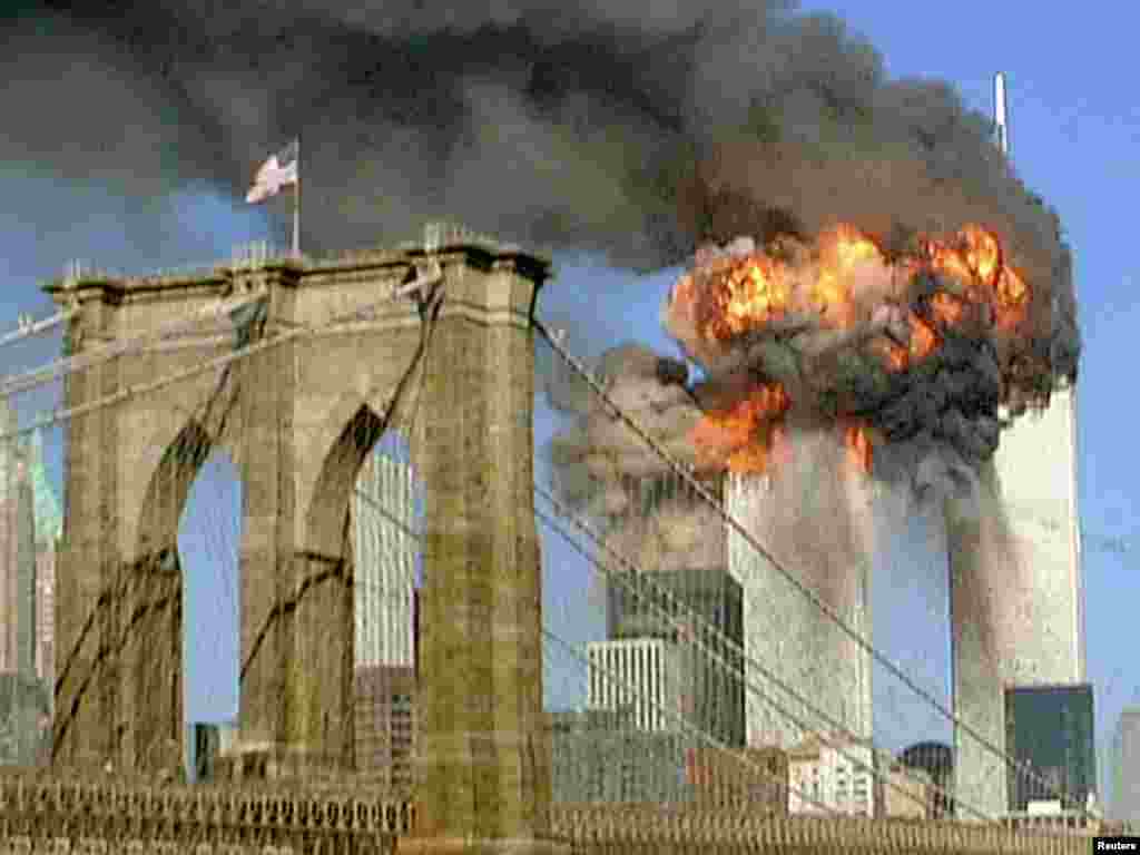 Turnurile de la World Trade Center arzînd văzute din spatele podului Brooklyn, la 11 septembrie 2001.