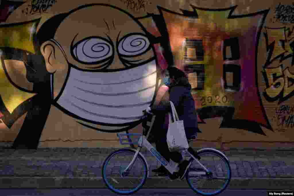 Жена с маска минава с колело пред графит, нарисуван на строеж в Шанхай, Китай, на 17 февруари.