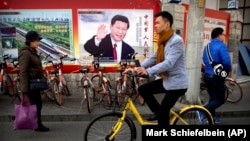 Люди проходят мимо рекламного щита, на котором изображен китайский президент Си Цзиньпин, Китай, Пекин, 2 марта 2018 года