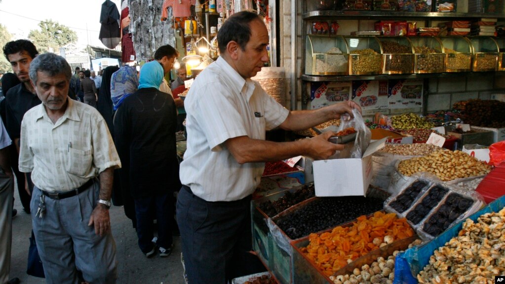 A shopkeeper works at his shop, as people pass, at the Tehran's old main Bazaar, Iran, Monday, Sept. 1, 2008