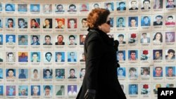 An woman walks past a wall in Pristina on January 25 of photos depicting people missing since the 1998-99 conflict in Kosovo.