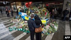 People stand in front of a flower-covered police car as they observe a minute of silence on April 10 at the site where a truck drove into a department store in Stockholm.