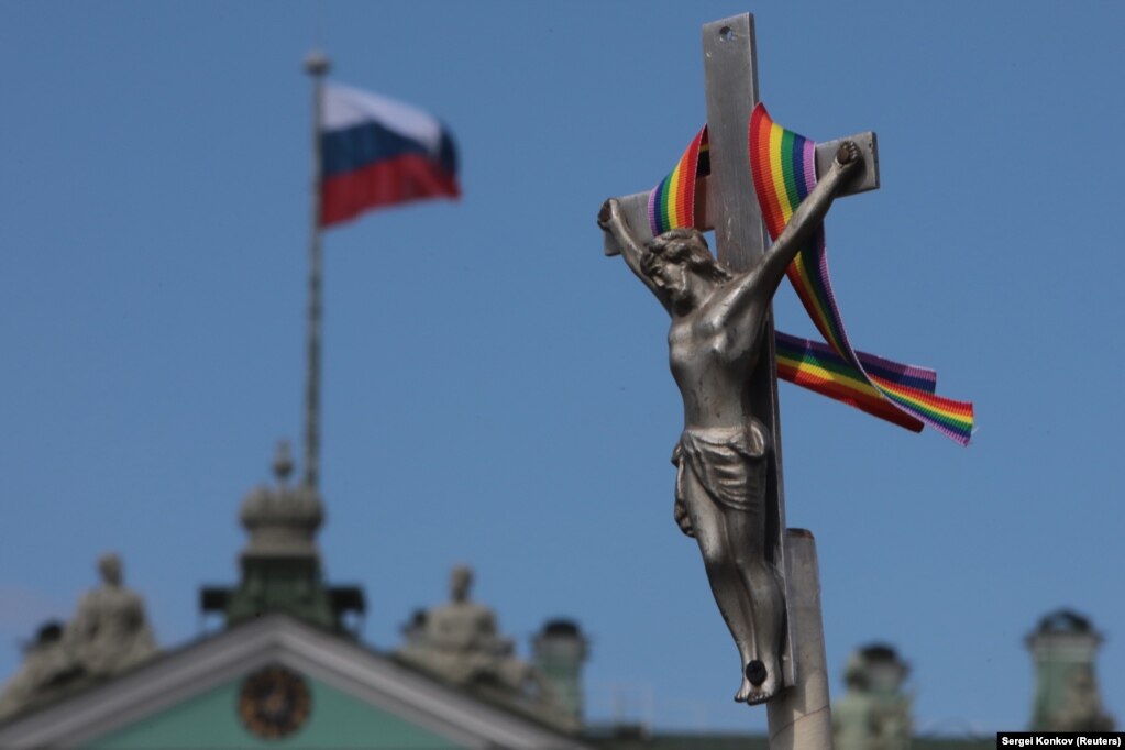 NjÃ« shirit me ngjyra tÃ« ylberit Ã«shtÃ« lidhur pranÃ« njÃ« kryqi, gjatÃ« njÃ« parade tÃ« komunitetit LGBT nÃ« ShÃ«n Petersburg.