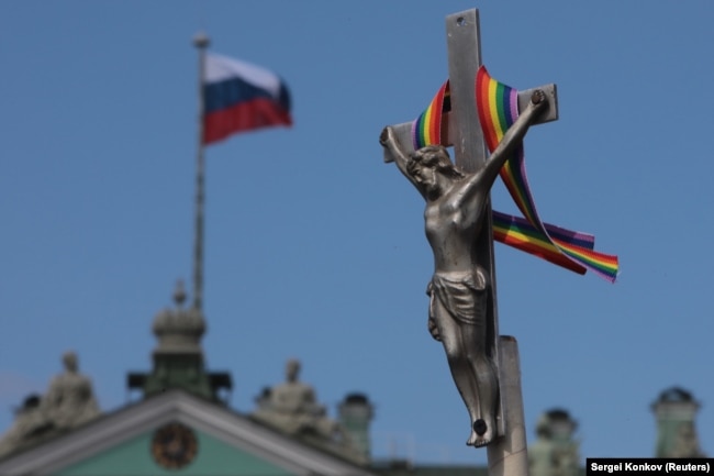 A rainbow-colored ribbon is tied to a crucifix next to a Russian flag fluttering atop the State Hermitage Museum in St. Petersburg last month.