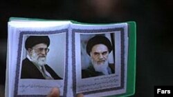 Irán – Egy férfi, kezében egy könyv Homeini ajatollah (jobbra) és Ali Hámenei ajatollah portréival. Dátum nélkül