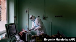 Un doctor ucrainean care poartă un costum special pentru a se proteja de coronavirus, ajută un pacient cu masca de oxigen la o unitate de terapie intensivă dintr-un spital regional din Ucraina.