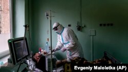 Український лікар у захисному костюмі від коронавірусу допомагає пацієнту з кисневою маскою в реанімаційному відділенні обласної лікарні в Україні (архівне фото)