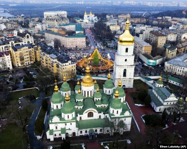 У Києві до новорічно-різдвяних свят підготували спеціальний маршрут, який з'єднав три локації. На кожній з них є своя новорічна ялинка. Локації облаштовані на Софійській і Контрактовій площах, а також біля Арки дружби народів. На фото на передньому плані Софійський собор – пам’ятка української архітектури і монументального живопису, споруда часів України-Русі (1011 рік). Одна з найголовніших християнських святинь Східної Європи, історичний центр Київської митрополії. Ансамбль Софійського монастиря занесено до спадщини ЮНЕСКО