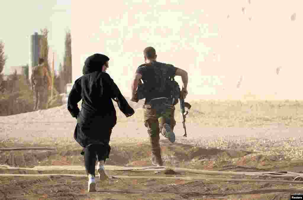 A woman reporter runs with a rebel fighter to avoid snipers at the frontline against Islamic State jihadists in northern Syria on October 10. (Reuters/Jalal Al-Mamo)