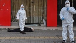 Медработники в защитных костюмах эвакуируют умершего на улице в Ухане рядом с одной из местных больниц, 30 января 2020 года
