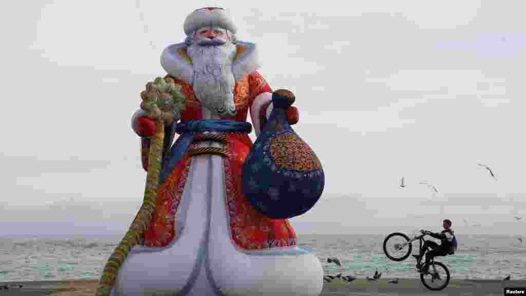 Велосипедист выполняет трюк на набережной в Алуште возле надувной фигуры Деда Мороза