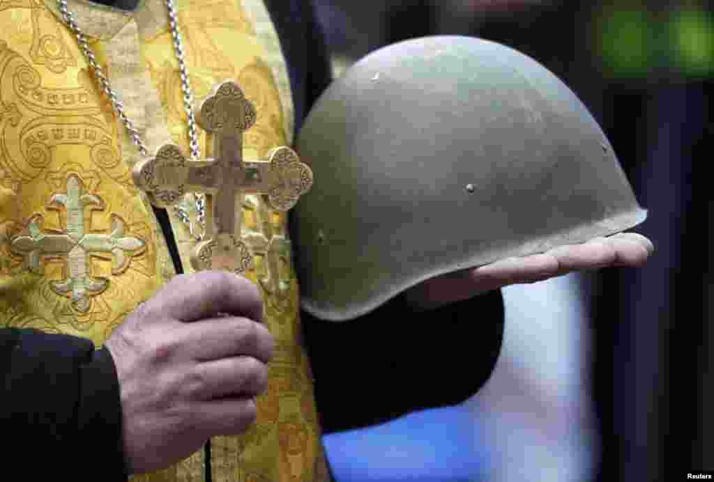 A priest holds a cross and a combat helmet during a funeral service for two antigovernent protesters.