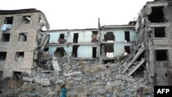 Armenia - 22-year-old Aida carrying water past a building left half destroyed by the earthquake in Gyumri, November 19, 2013