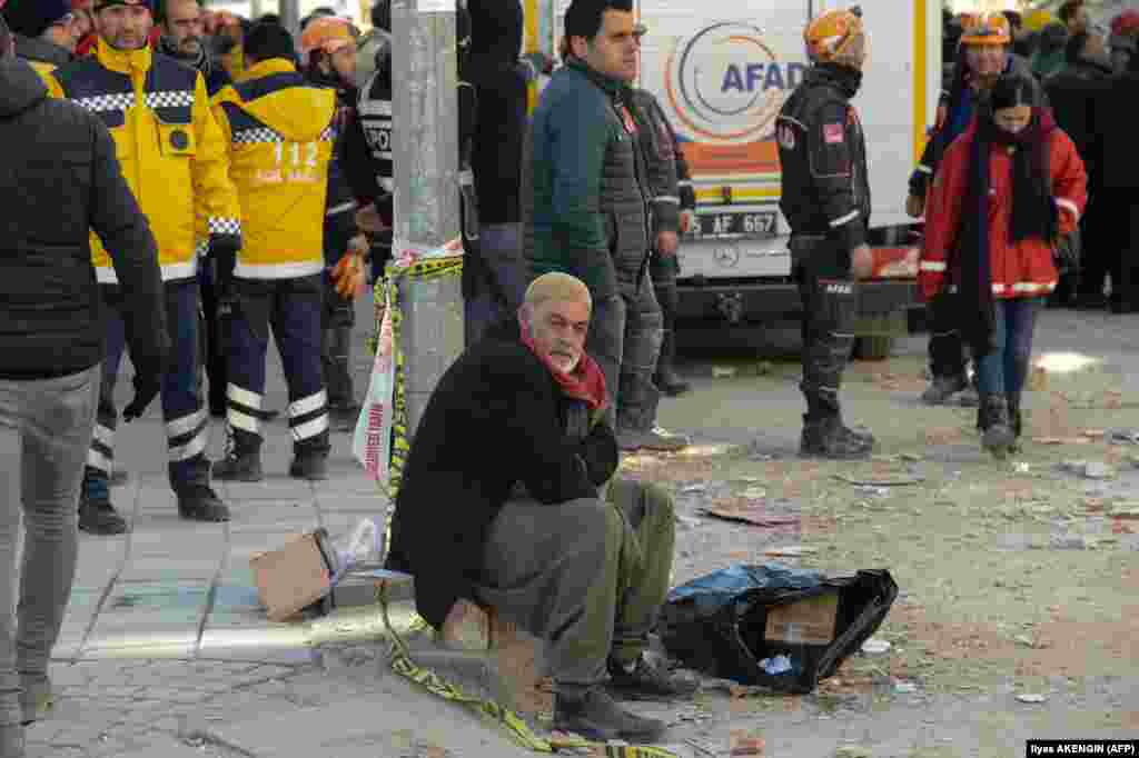 Muškarac sedi i gleda spasioce kako izvlače preživele iz ruševina