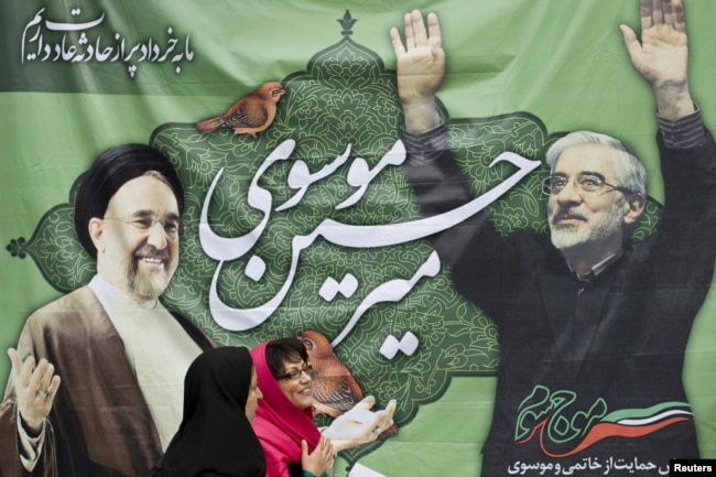 A photo from 2009 showing women walking past a picture of then presidential candidate Mir Hossein Musavi (right) and former President Mohammad Khatami in Tehran.