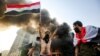 A masked protester flashes the victory gesture as he waves an Iraqi national flag before a burning building during a demonstration against state corruption and poor services on October 1.