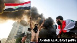 A masked protester flashes the victory gesture as he waves an Iraqi national flag before a burning building during a demonstration against state corruption and poor services on October 1.