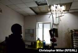 An employee inspects a hole left in the roof of an Avdiyivka auto parts store after an artillery shell came crashing through.