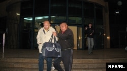 Мухтар Алиев (слева) в сопровождении встретившего его в аэропорту Алматы мужчины идет к ожидающей их автомашине. Алматы, 4 октября 2009 года. 