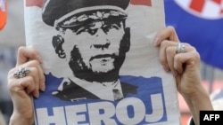 Një grua mban një gazetë me portretin e gjeneralit kroat, Ante Gotovina, ku shkruan “hero”, ndërsa ndjek transmetimin e drejtpërdrejtë televiziv të aktgjykimit ndaj tij. Zagreb, 15 prill 2011.