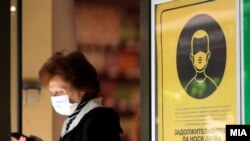 Илустрација - Жителка на Скопје со заштитна маска поминува покрај плакат со предупредување за задолжително носење заштита за лице во затворени јавни објекти.